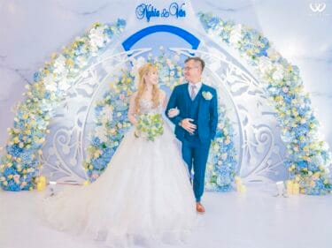 A bride and groom standing in front of a blue and white floral arch.
